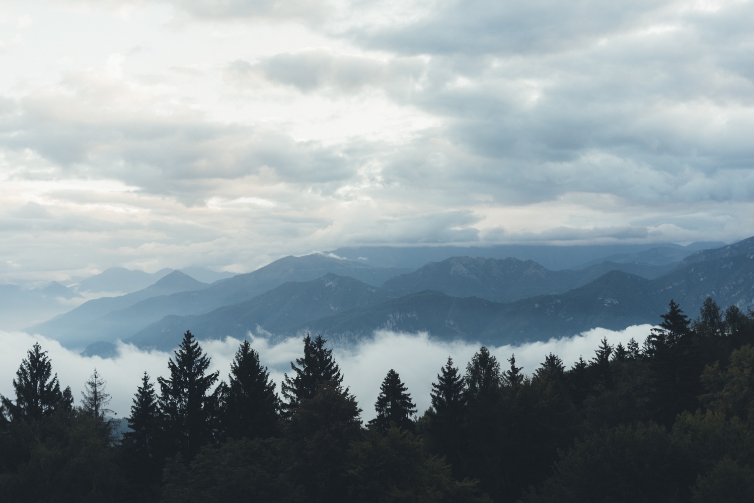 Clouds and low fog drift over forested mountain ridges.