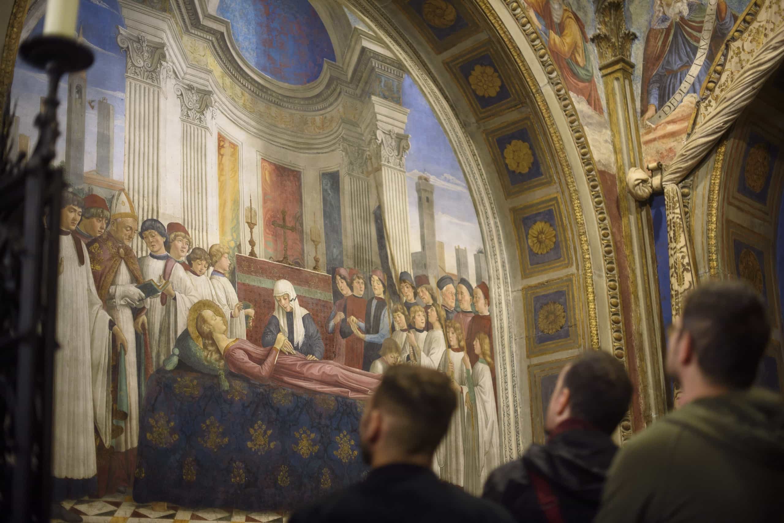 Alcuni membri del team di Moze osservano un affresco rinascimentale raffigurante la morte della Vergine Maria, con numerosi personaggi in abiti liturgici e architettura classica sullo sfondo.